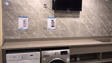 A laundry area with two washing machines, a television mounted on the wall, and informational posters on the wall.