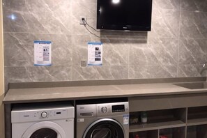 Un área de lavandería con dos lavadoras, un televisor montado en la pared y carteles informativos.