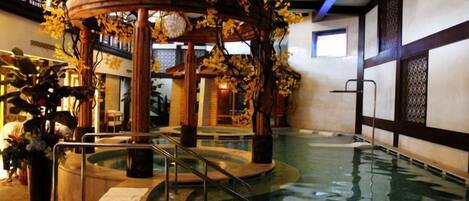 An indoor swimming pool with a wooden gazebo, surrounded by potted plants.