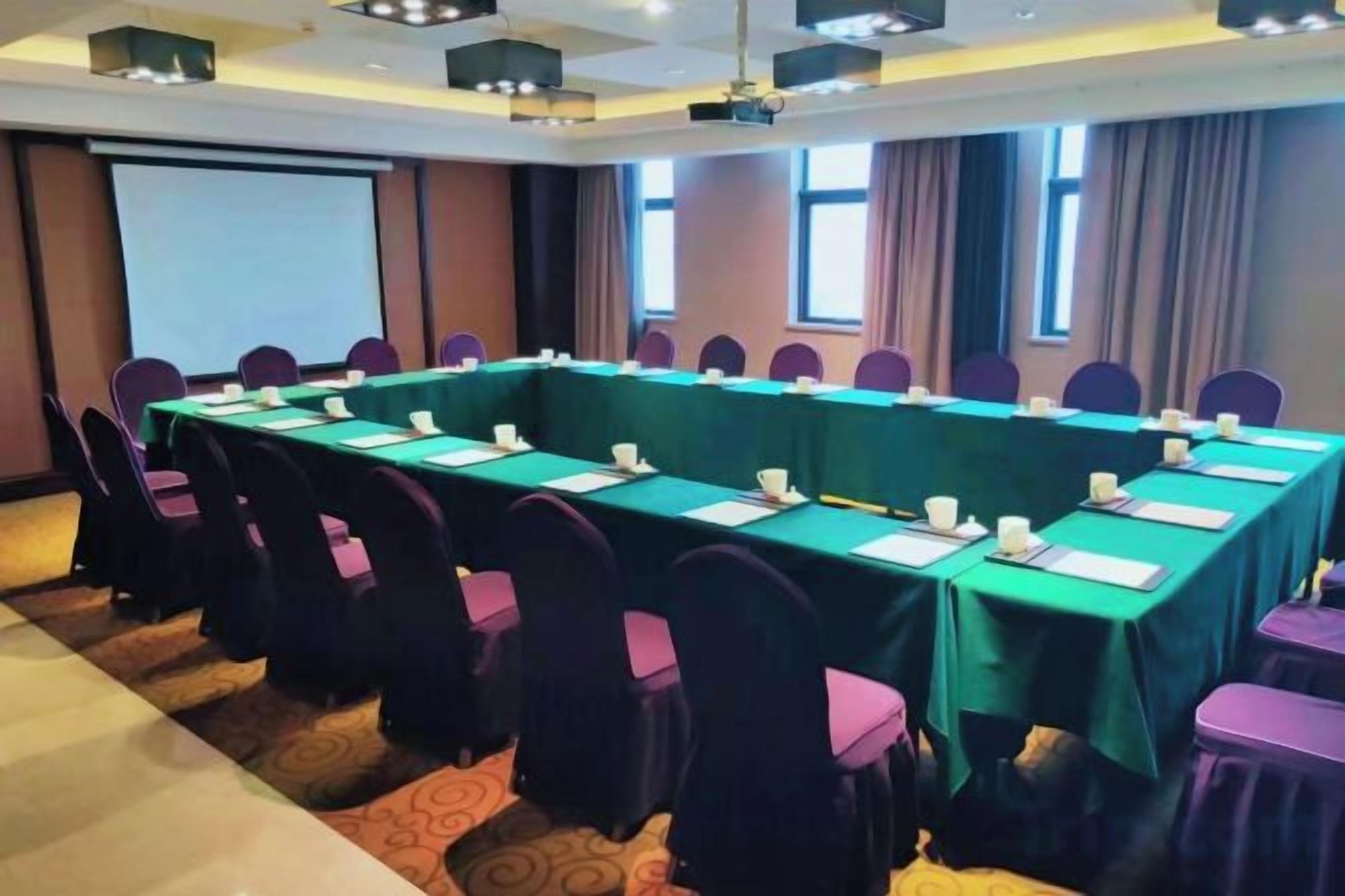 Un salón de conferencias con una larga mesa, sillas y una pantalla de proyector.