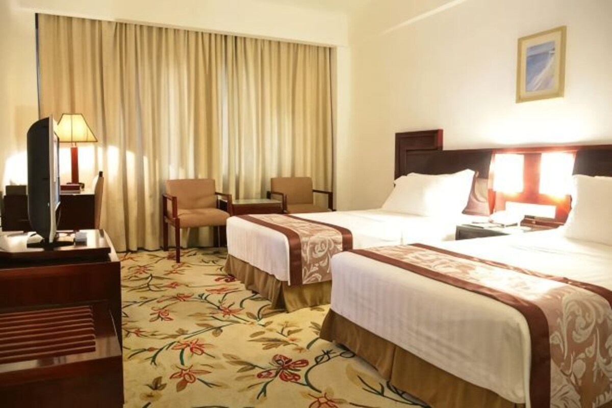 A hotel room with two beds, a desk, a chair, a TV, and a large window with curtains.