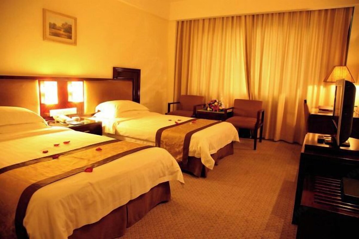 Een hotelkamer met twee bedden, een bureau, een stoel, een televisie en een raam met gordijnen.