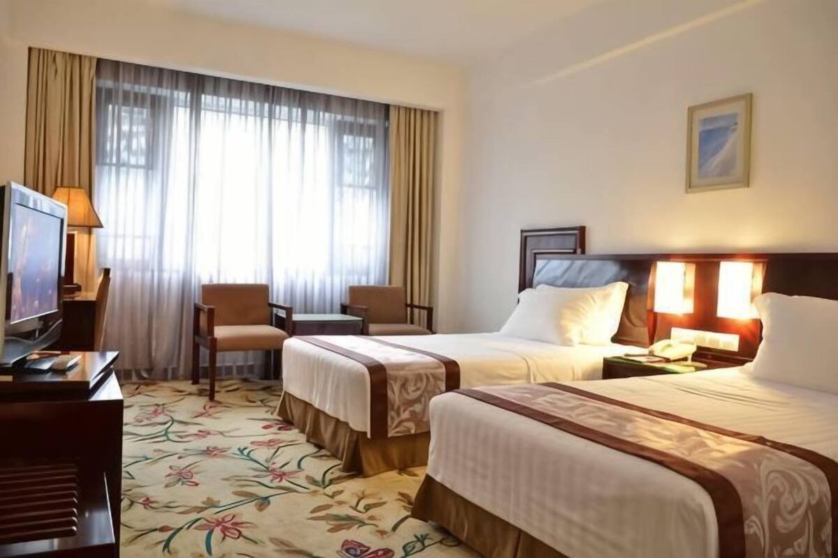 Une chambre d’hôtel avec deux lits, un bureau, une télévision et une grande fenêtre avec des rideaux.