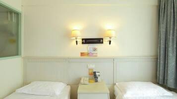 A hotel room with two single beds, a small bedside table with a lamp, and a wall-mounted light fixture.