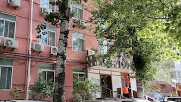 A multi-story building with air conditioning units, a tree, and parked cars.