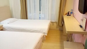 Ett hotellrum med två sängar, ett skrivbord, en tv och ett fönster med gardiner.