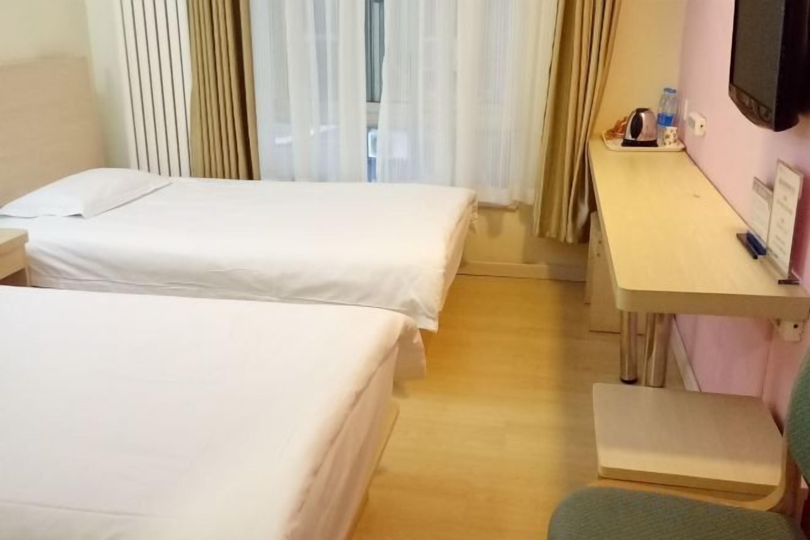 Habitación de hotel con dos camas, un escritorio, una silla y un televisor.