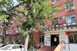 En byggnad med en röd fasad, flera fönster och en trappa som leder upp till entrén. Ovanför entrén finns en skylt med kinesiska tecken och siffran ’23’.