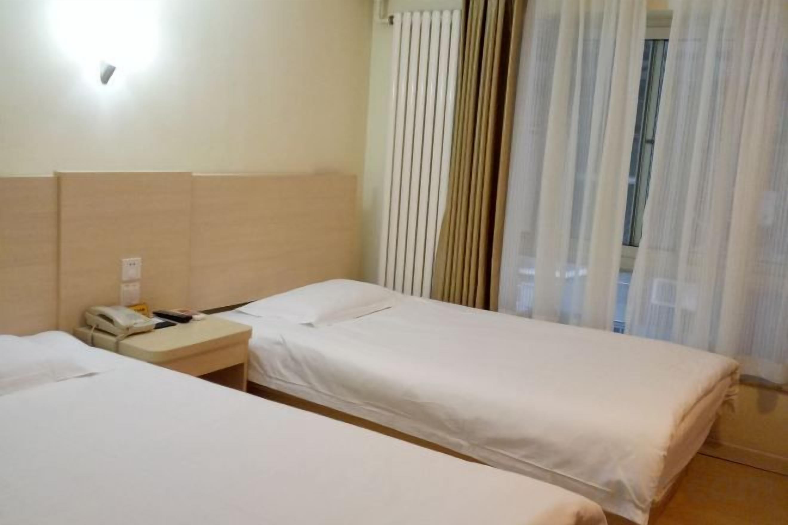 Habitación de hotel con dos camas individuales, una mesita de noche con teléfono y una ventana con cortinas traslúcidas.