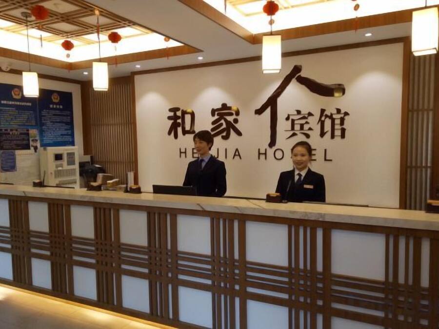 A reception desk with a sign reading 'HEJIA HOTEL' and two staff members behind it.