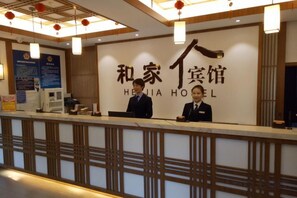 A reception desk with a sign reading 'HEJIA HOTEL' and two staff members behind it. - Hejia Inn (Beijing Fuwai Hospital) (Beijing)