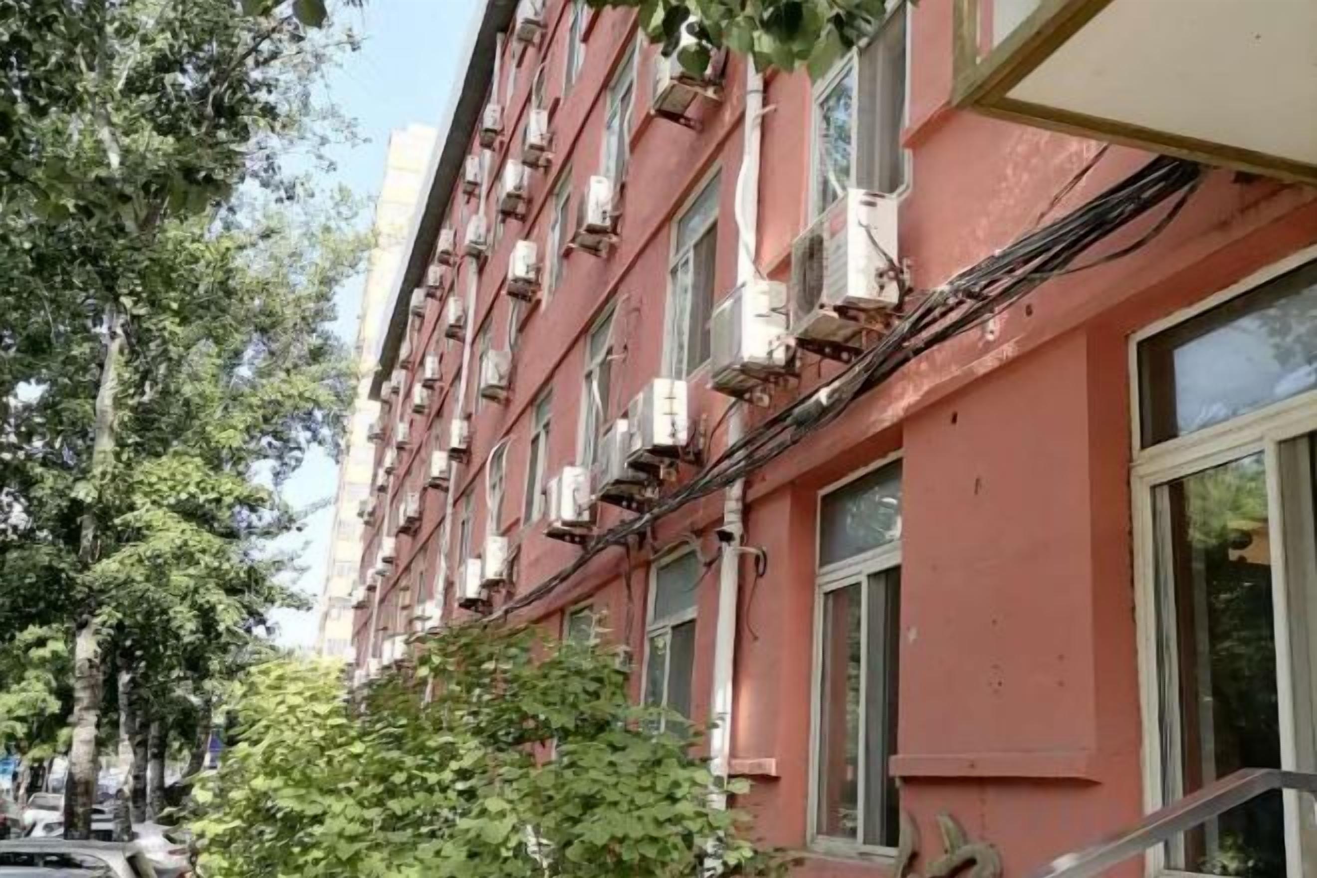 A multi-story building with external air conditioning units, a visible staircase, and a tree in the foreground.