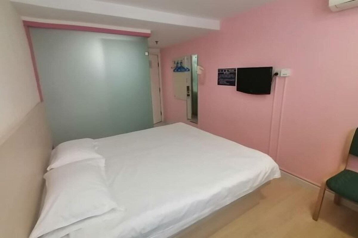 A bedroom with a bed, a chair, a wall-mounted air conditioner, and a door.