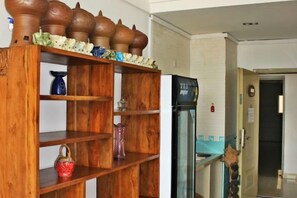 Una estantería de madera con varios objetos decorativos, un refrigerador y una puerta que da a otra habitación.