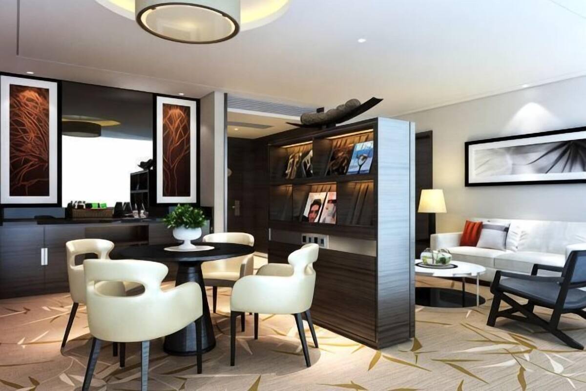 A modern hotel room with a dining area, a sofa, a bookshelf, and a large window.