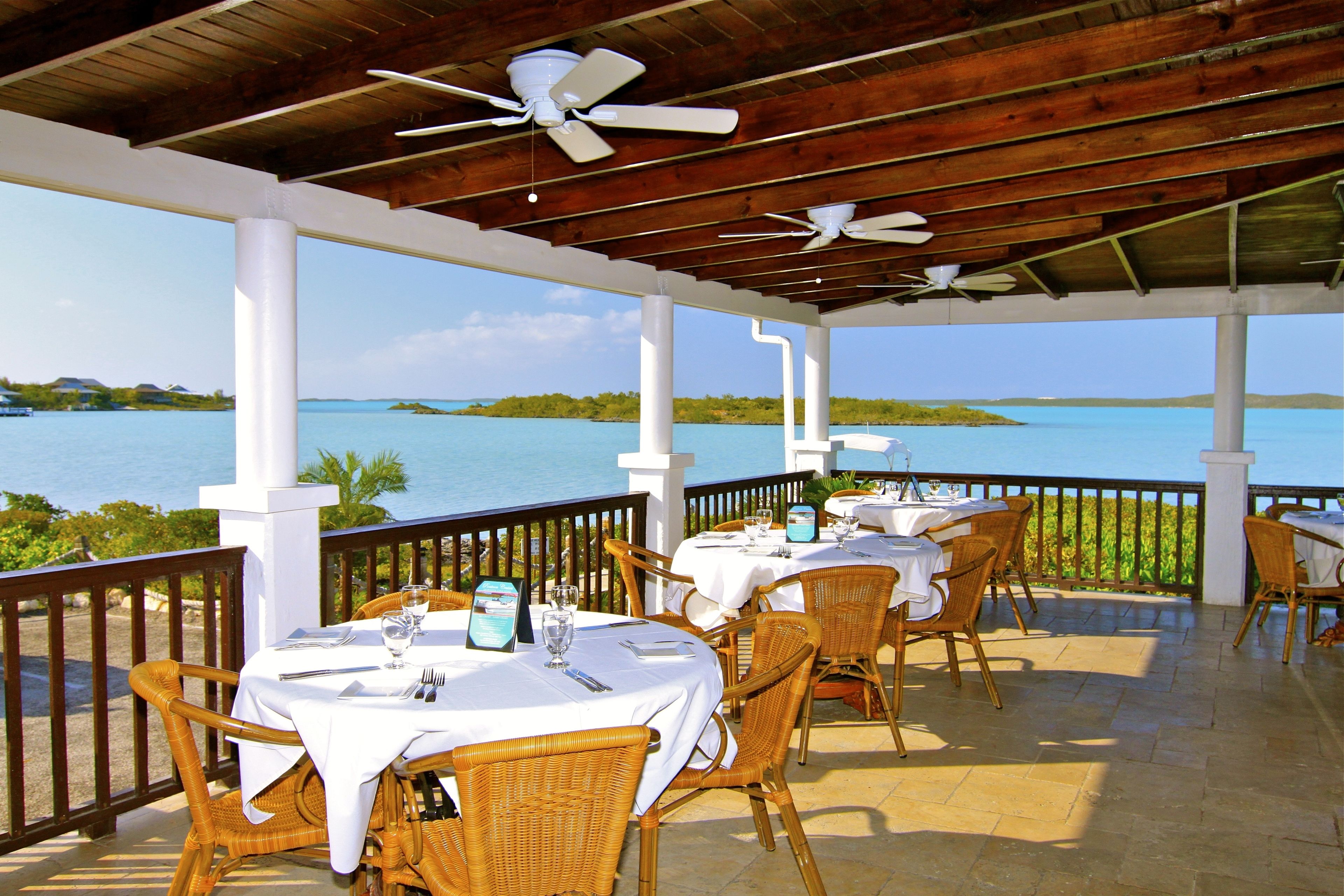 Un'area pranzo all'aperto con tavoli e sedie, un soffitto in legno e vista sul mare.