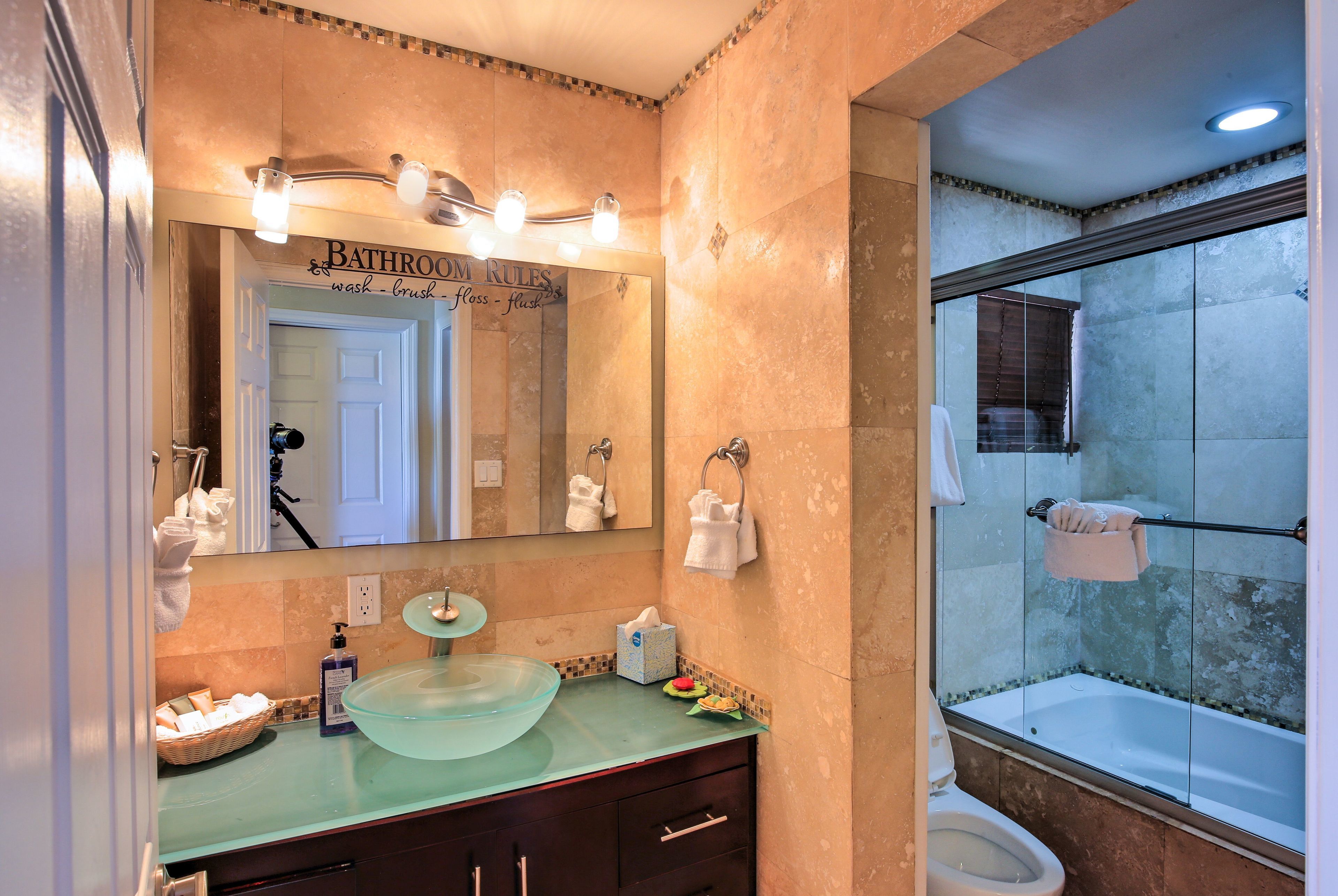 Un baño con lavamanos de vidrio, un espejo grande y zona de ducha.