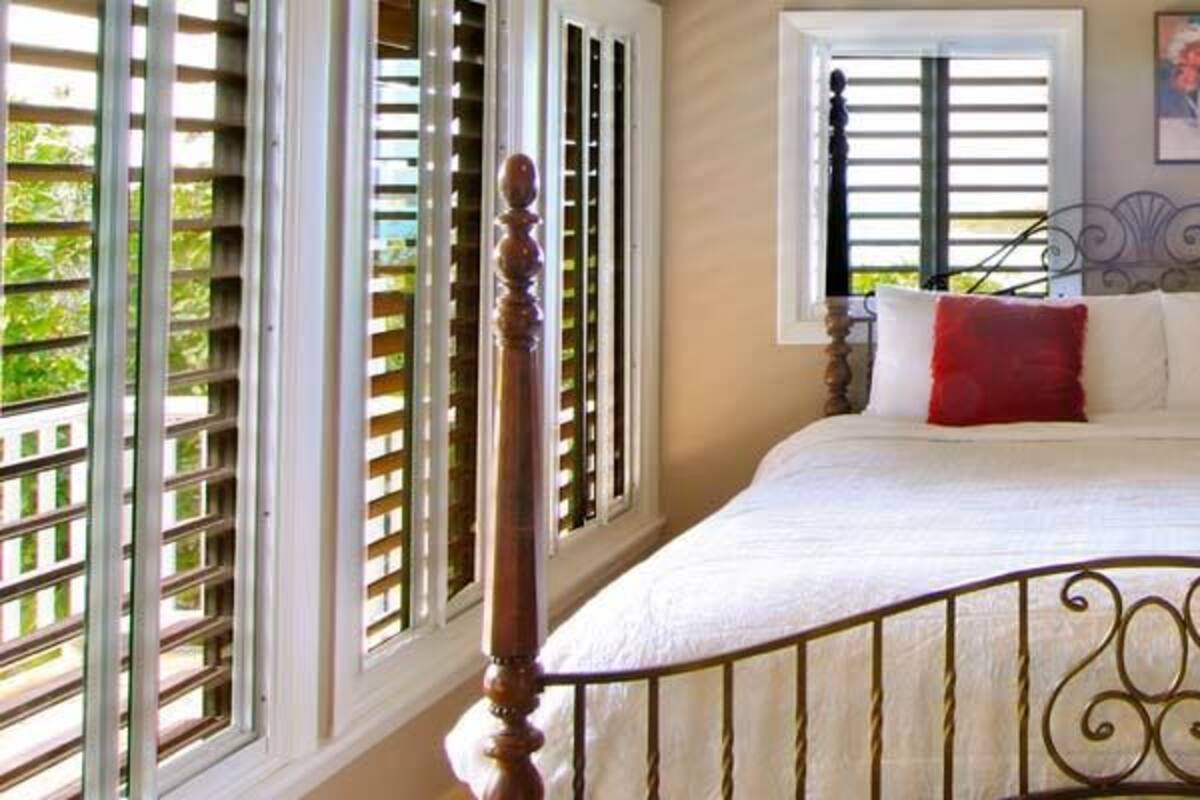 Quarto com uma cama, duas janelas com persianas, uma mesa de cabeceira e um abajur.
