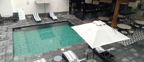 Un área de piscina con sillones de descanso, sombrillas y un bar.