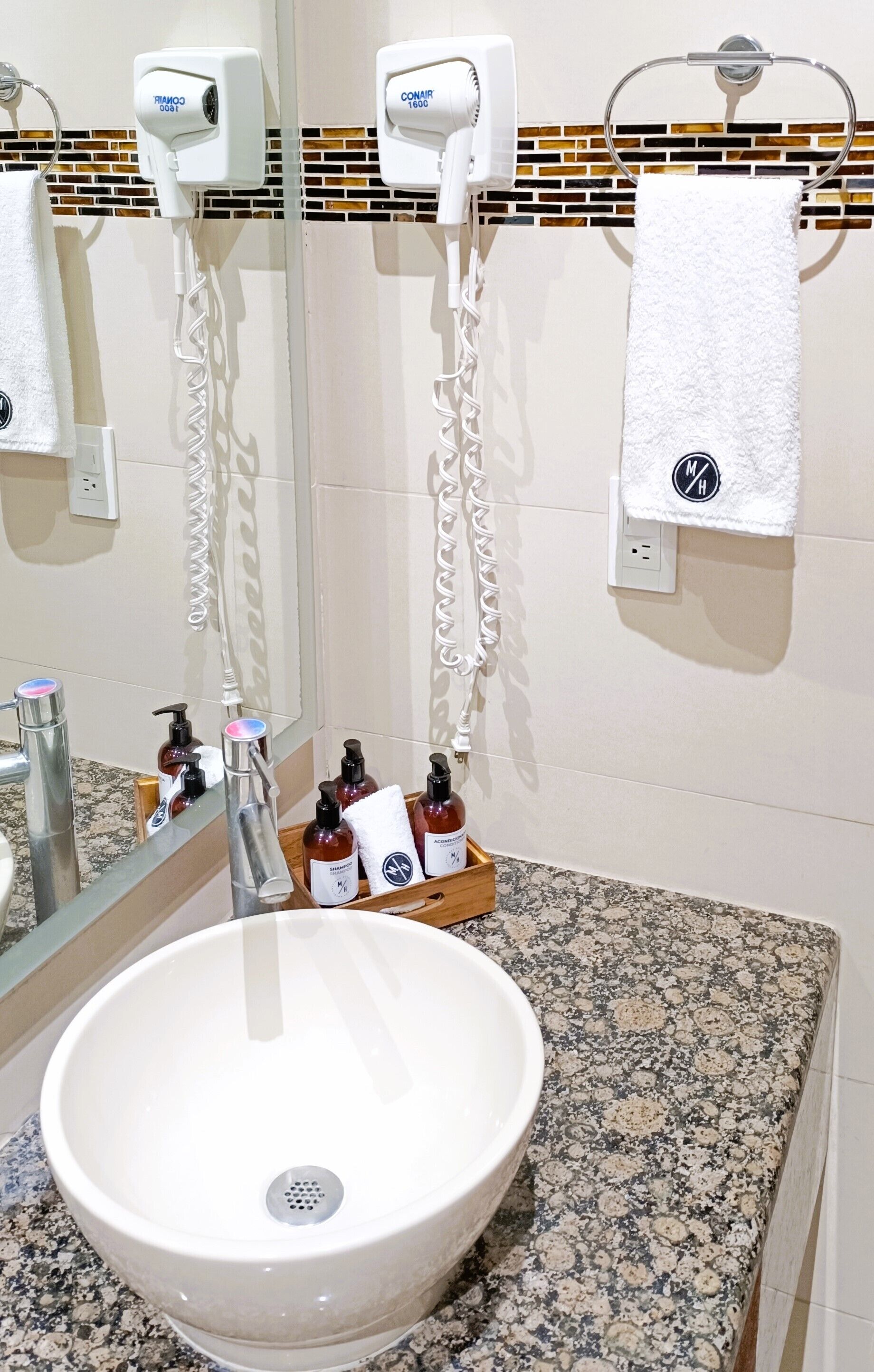 Un baño con lavamanos blanco, espejo, toallero y secadores de pelo.