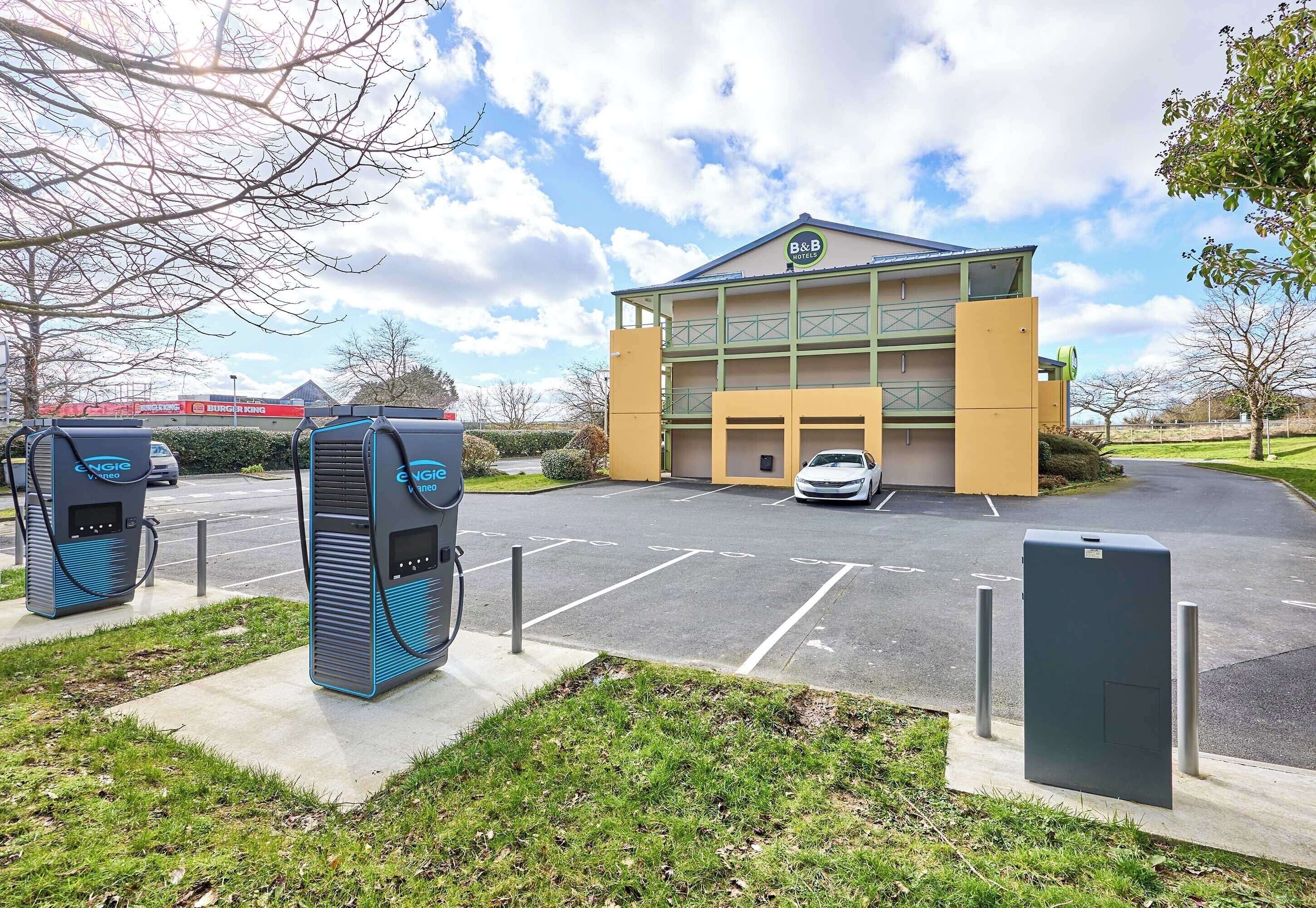 Un hôtel doté d’un parking, de bornes de recharge pour véhicules électriques et d’un bâtiment portant une enseigne.