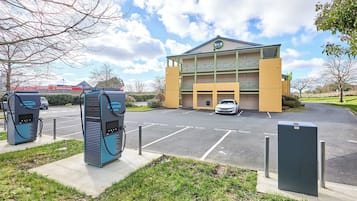 Un hotel con estacionamiento, puntos de recarga para vehículos eléctricos y un edificio con un cartel.