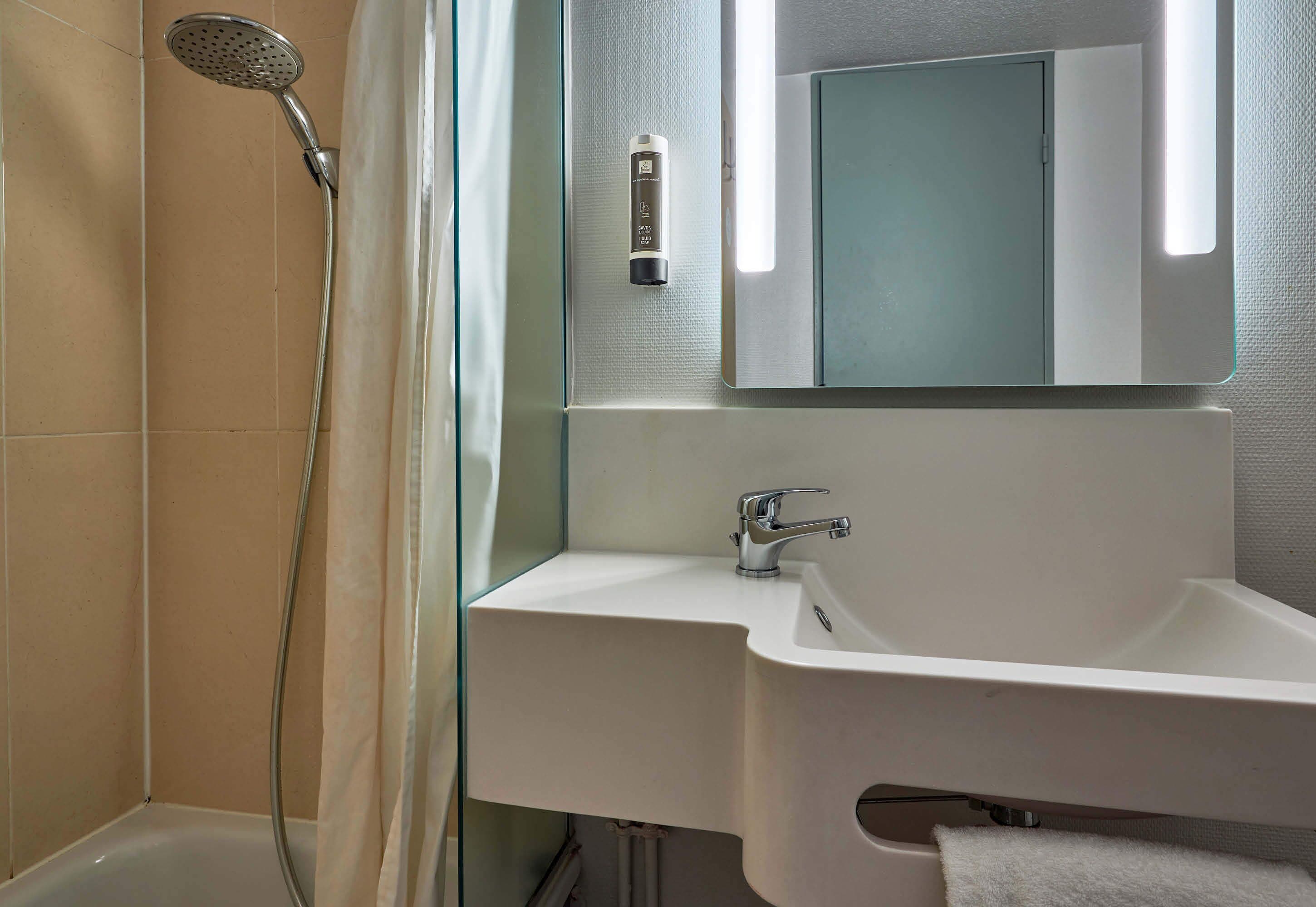 Une salle de bain équipée d’une douche, d’un lavabo, d’un miroir et d’un porte-serviettes.