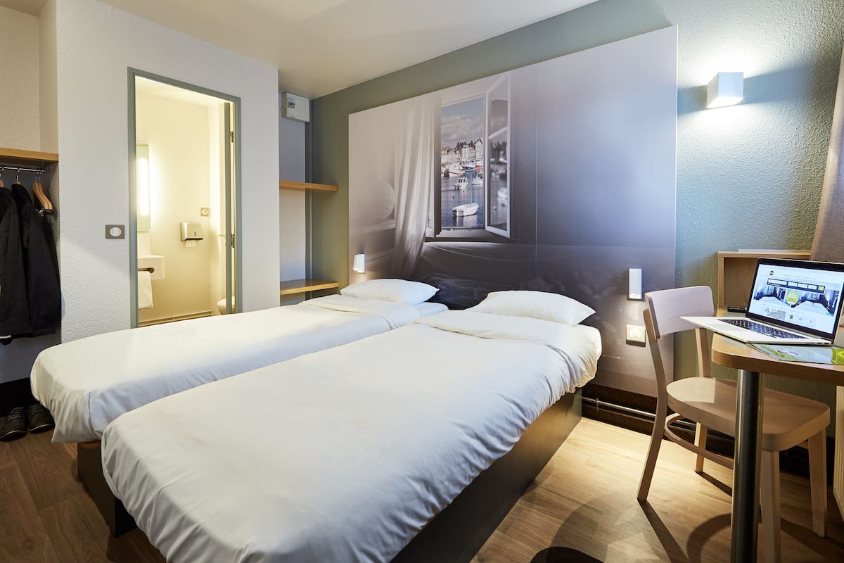 Une chambre d’hôtel avec deux lits, un bureau avec un ordinateur portable, une chaise et une grande fenêtre donnant sur le port.