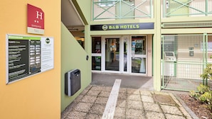Entree van een B&B hotel met een welkomstbord, een informatiebord en een rolstoeltoegankelijk pad.