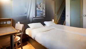 Een hotelkamer met een bed, een bureau, een stoel, een raam met uitzicht op een gebouw en een trap.
