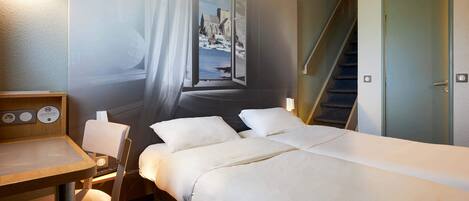 Habitación de hotel con cama, escritorio, silla, ventana con vista a un edificio y una escalera.