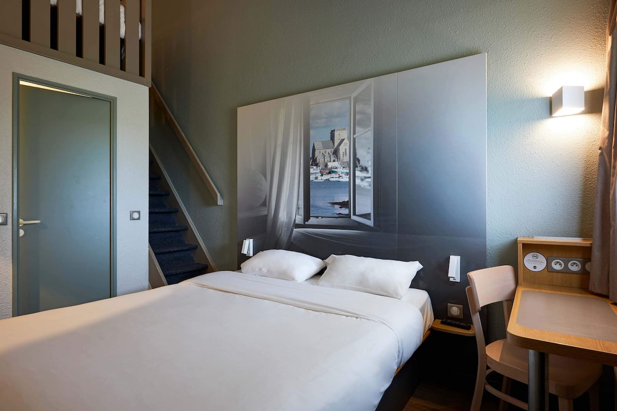 Une chambre d’hôtel équipée d’un lit, d’un bureau, d’une chaise, d’un escalier et d’une lampe fixée au mur.