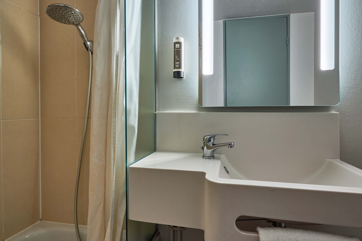 Une salle de bain équipée d’une douche, d’un lavabo, d’un miroir et d’un porte-serviettes.