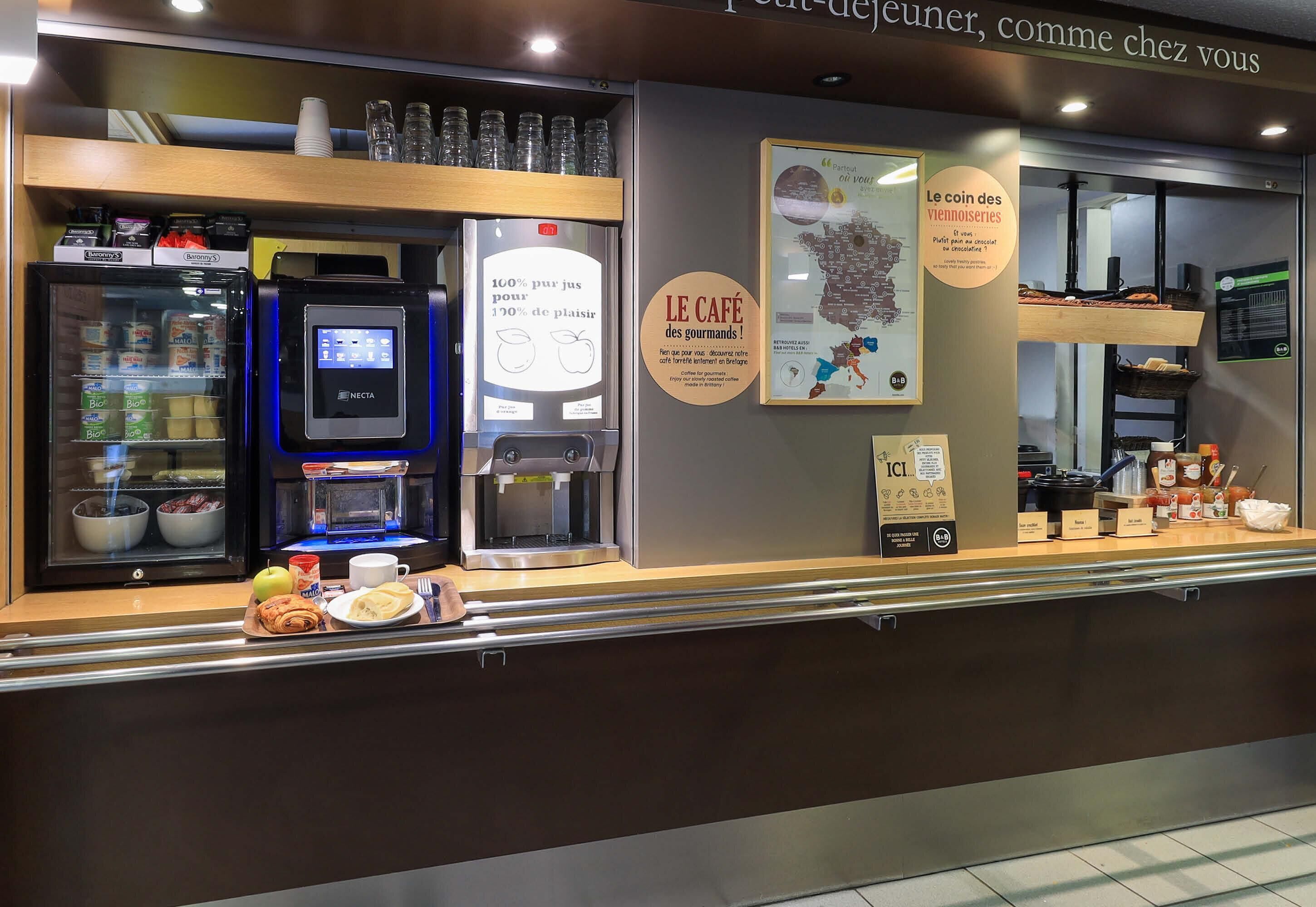 Een café toonbank met een drankenspender, een koelvitrine en een menubord.