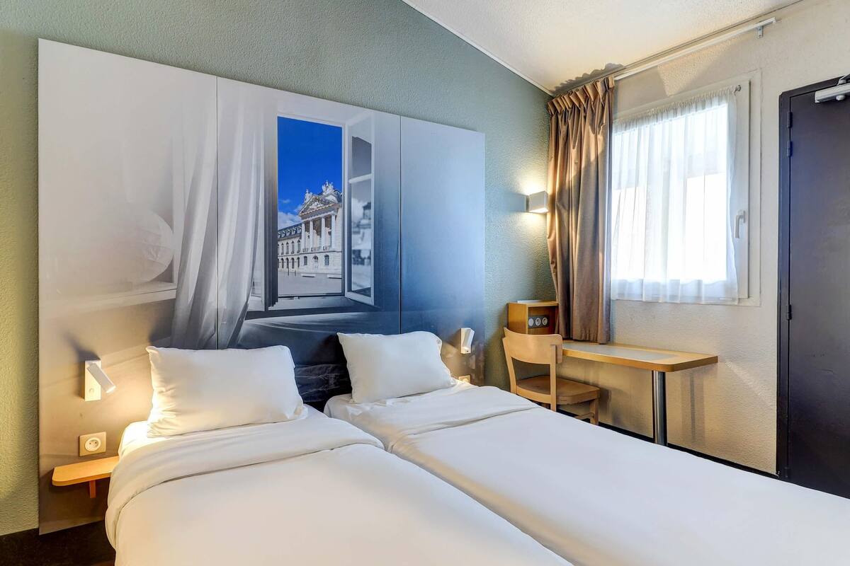 Habitación de hotel con una cama grande, un escritorio, una silla, una mesita de noche y un televisor montado en la pared.