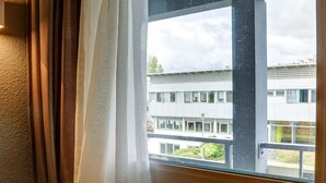 Una habitación con un ventanal amplio, cortinas y vista a un edificio de varios pisos.