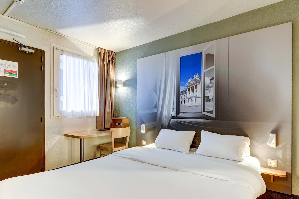 Ein Hotelzimmer mit einem Bett, einem Schreibtisch, einem Sessel, einem an der Wand montierten Fernseher und einer Tür mit einem Schild.