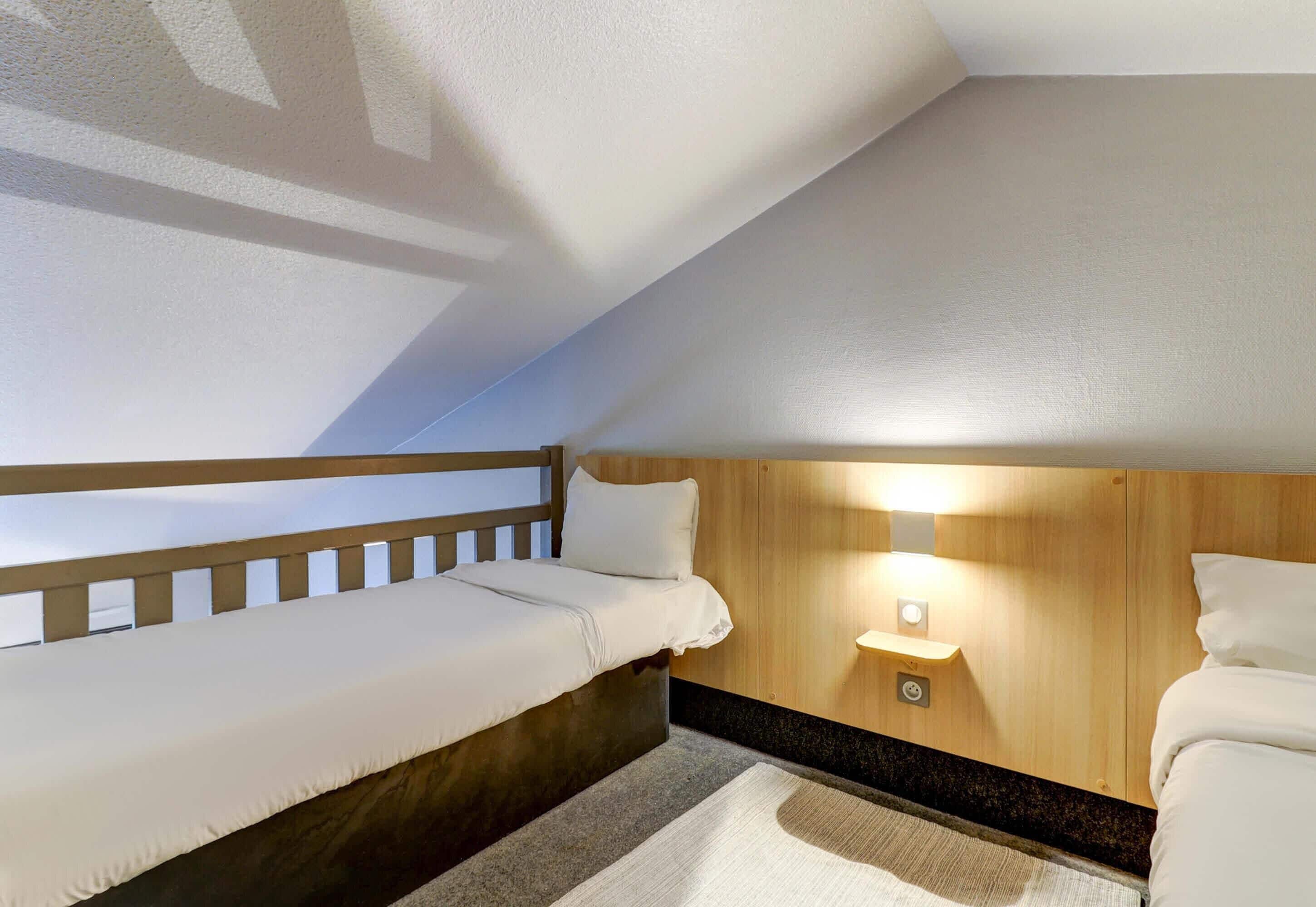 Une petite pièce agréable et chaleureuse, avec un lit superposé, une table de chevet avec une lampe et une tête de lit en bois.