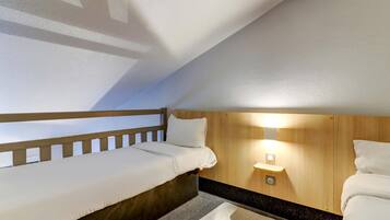 A small, cozy room with a bunk bed, a bedside table with a lamp, and a wooden headboard.