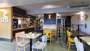 Un interior de restaurante con mesas y sillas, una barra con una máquina de café y una pizarra de menú.