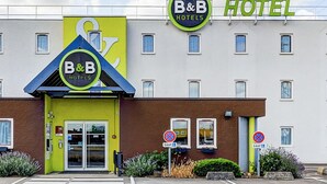 A B&B hotel with a bright yellow facade, a large sign, and a parking area with no parking signs. - B&B HOTEL DIJON Les Portes du Sud (Acti-Sud) (Marsannay-la-Cote)