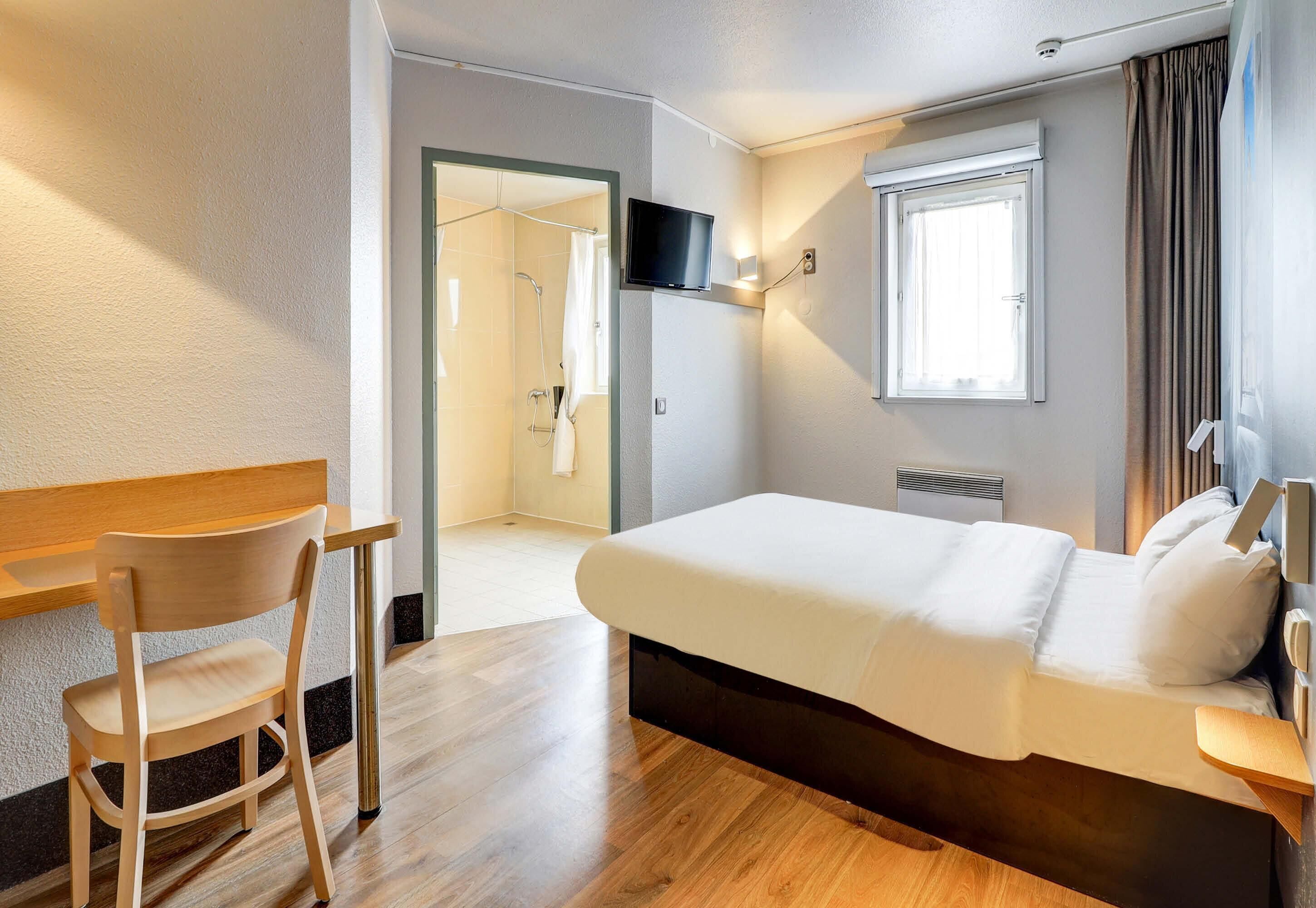 Une chambre d’hôtel avec un lit, une télévision, un bureau et une chaise.