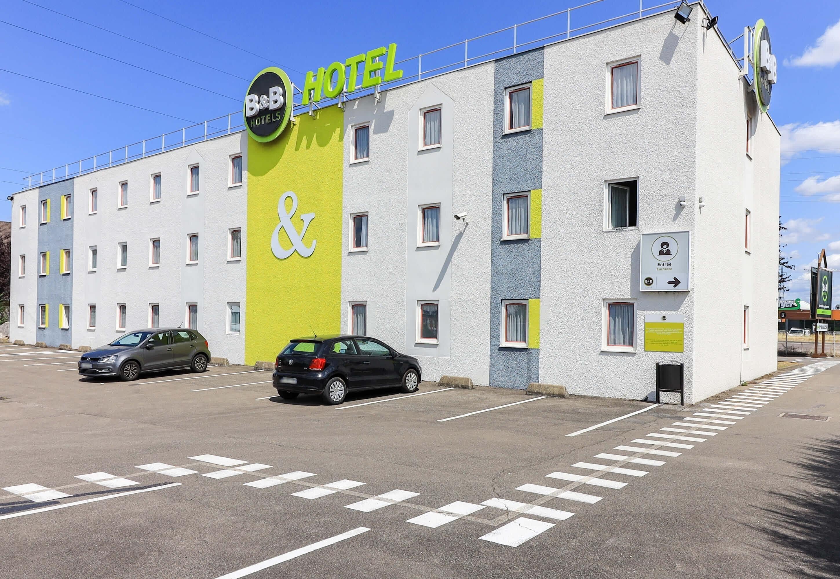 A B&B hotel with a colorful facade, a parking lot, and a clear sky.