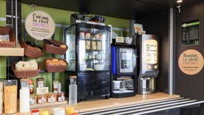 A breakfast bar with a refrigerator, coffee machine, and baskets of bread. - B&B HOTEL DIJON Les Portes du Sud (Acti-Sud) (Marsannay-la-Cote)