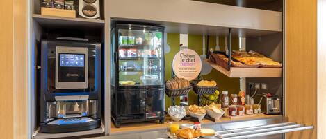 Un bufé de desayuno con una máquina de café, sección refrigerada y diversos alimentos.