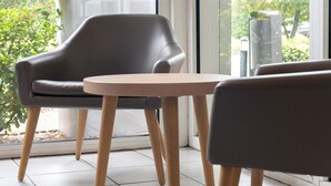 Habitación moderna con un ventanal grande, un sillón de cuero gris, una mesa redonda de madera y vistas a zonas verdes.