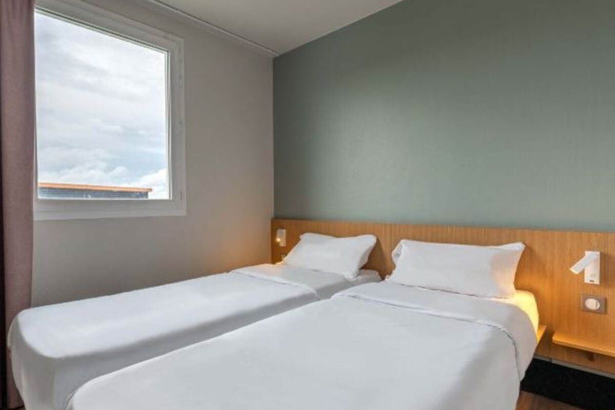 Une chambre d’hôtel avec deux lits simples, une grande fenêtre et une vue sur le ciel.