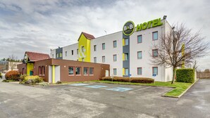 A B&B hotel with a modern design, featuring a prominent logo, multiple windows, and a parking area. - B&B HOTEL Goussainville CDG (Goussainville)