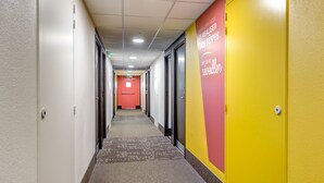 A hallway with a red door at the end, white walls, and a yellow accent wall with text. - B&B HOTEL Goussainville CDG (Goussainville)