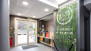 A hotel reception area with a glass door entrance, a reception desk, a wall with greenery, and a security rope. - B&B HOTEL Goussainville CDG (Goussainville)